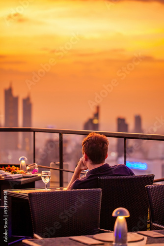 Photography Young man with glass of wine rest at luxury rooftop restaurant watching orange sky sunset
