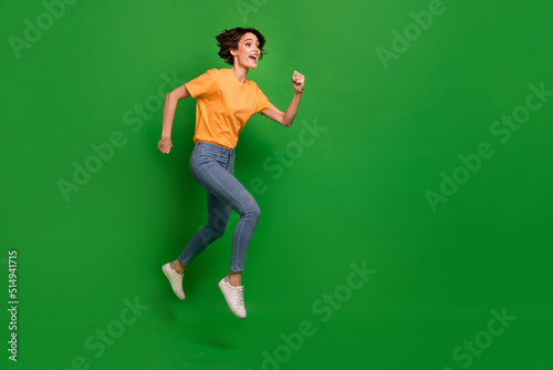 Full size profile portrait of active energetic girl run jump look empty space isolated on green color background
