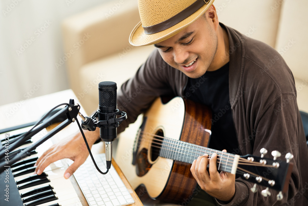 Obraz premium Professional Musician with condenser microphone and tablet for Mixing Mastering music. Hispanic male composing a song with guitar and piano keyboard at digital Recording home studio