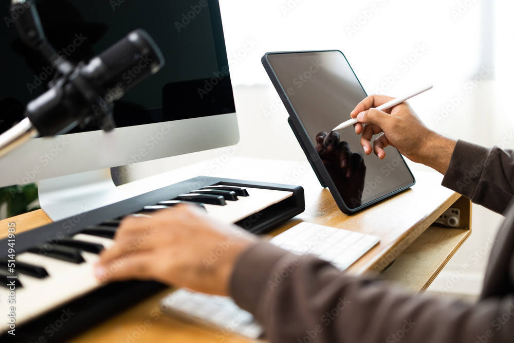 Close up hands song writer composing music note on tablet. Professional composer Recording Mixing and Mastering in home studio with keyboard and guitar. Digital music production Close up hands song writer composing music note on tablet. Professional composer Recording Mixing and Mastering in home studio with keyboard and guitar. Digital music production