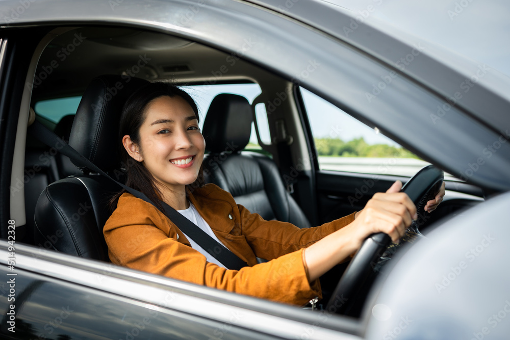 Young beautiful asian women getting new car. she very happy and excited. Smiling female driving vehicle on the road on a bright day.