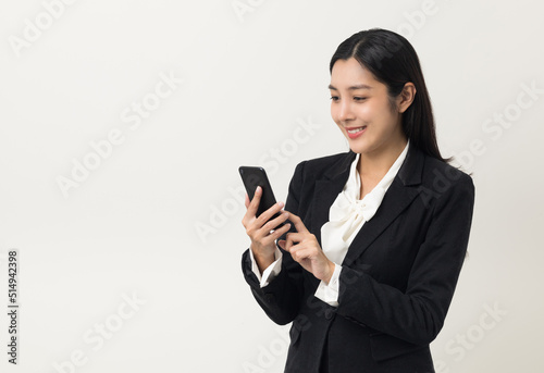 Happy young asian business woman using smartphone on isolated white background. Attractive female in suit holding cell phone feeling happy. Portrait shot in studio.