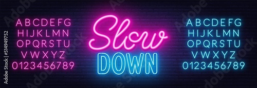 Slow Down neon lettering on brick wall background.