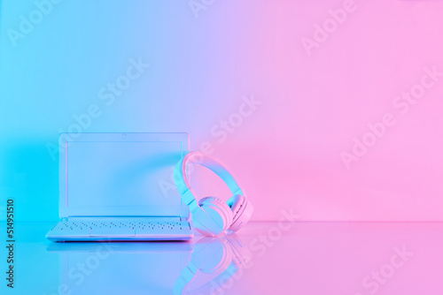 Office table with notebook computer and headphones in vibrant gradient holographic neon colors with copy space. Concept art. Minimal office surrealism.
