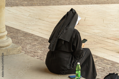 An elderly nun photographs gray stones of a vintage square on a smartphone, next to a second mobile phone, a bottle of water, a backpack, a touchscreen display of a mobile phone in a female hand photo