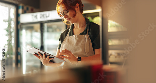 Cheerful store owner using a digital tablet in her grocery store photo