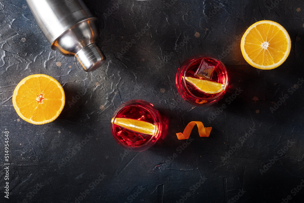 Campari cocktail with fresh oranges and a cocktail shaker, overhead flat lay shot on a black slate background with a place for text