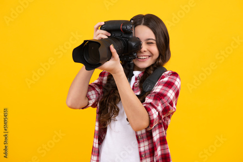Fotografie 12, 13, 14 year old teen girl holding digital camera or DSLR over yellow background