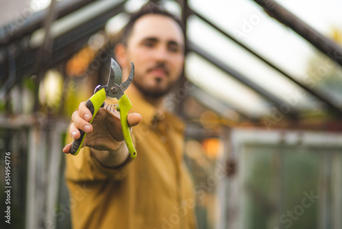 A man with a shovel and secateurs in his hands is sitting near a greenhouse. Farming. The process of caring for the greenhouse and seedlings. Rural life. Plant breeding and selection. photo