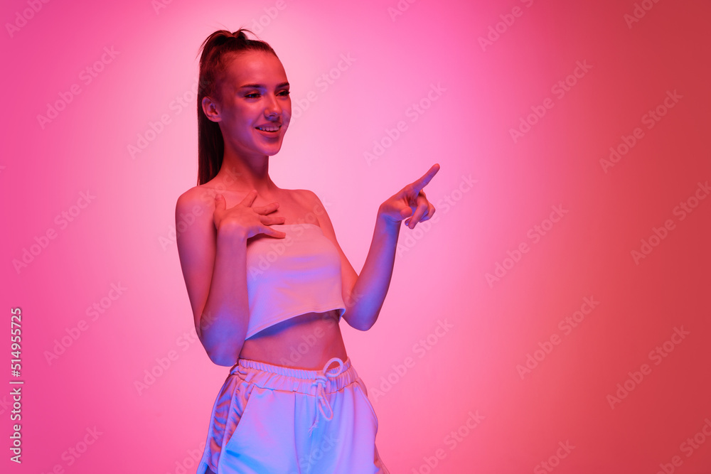 Happy young beautiful girl with long hair posing isolated on magenta color background in neon light. Concept of beauty, art, fashion, emotions, youth Happy young beautiful girl with long hair posing isolated on magenta color background in neon light. Concept of beauty, art, fashion, emotions, youth
