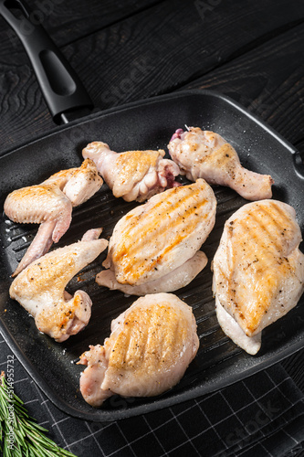 Roasted on a grill skillet chicken meat and chicken parts - drumstick, breast fillet, wing, thigh. Black wooden background. Top view