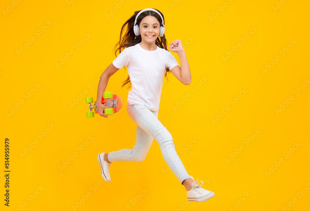 Jump and run. Teenagers youth casual culture. Teen girl with skateboard and headphones over isolated studio background. Teenager in fashion stylish clothes. Smiling girl.