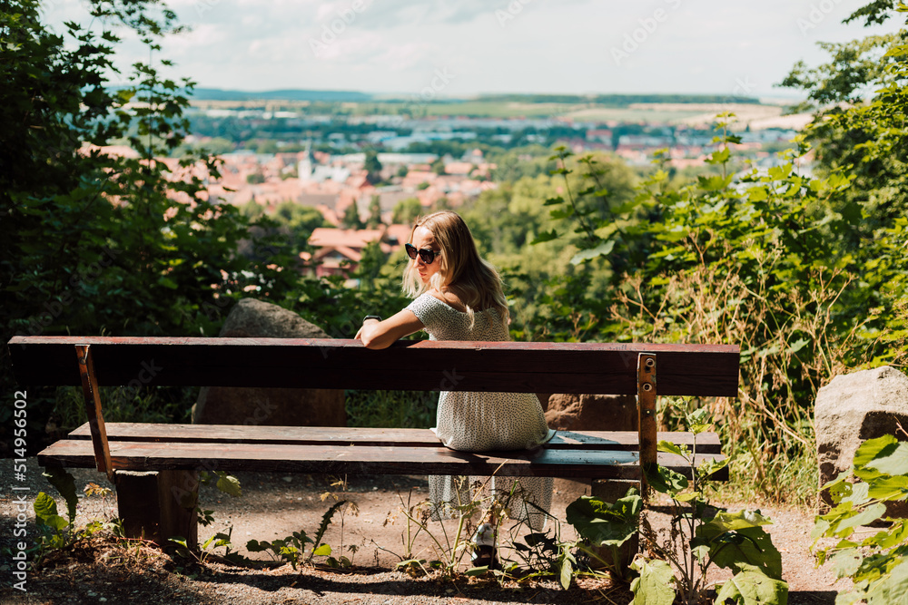 A woman sits with her back on a bench and looks at the city and the mountains