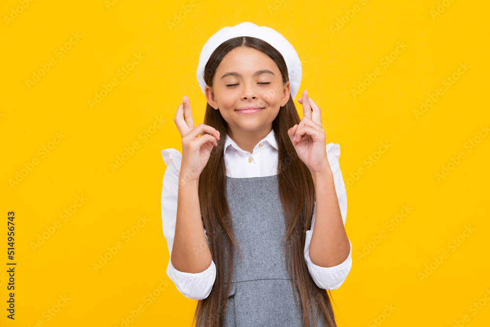 Funny teenager child holding fingers crossed for good luck. Girl prays and hopes dreams come true, isolated on yellow background. Funny teenager child holding fingers crossed for good luck. Girl prays and hopes dreams come true, isolated on yellow background.