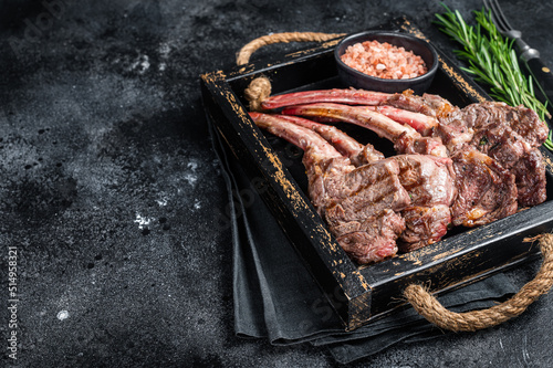 Grilled lamb chop steak, mutton meat cutlet in wooden tray. Black background. Top view. Copy space
