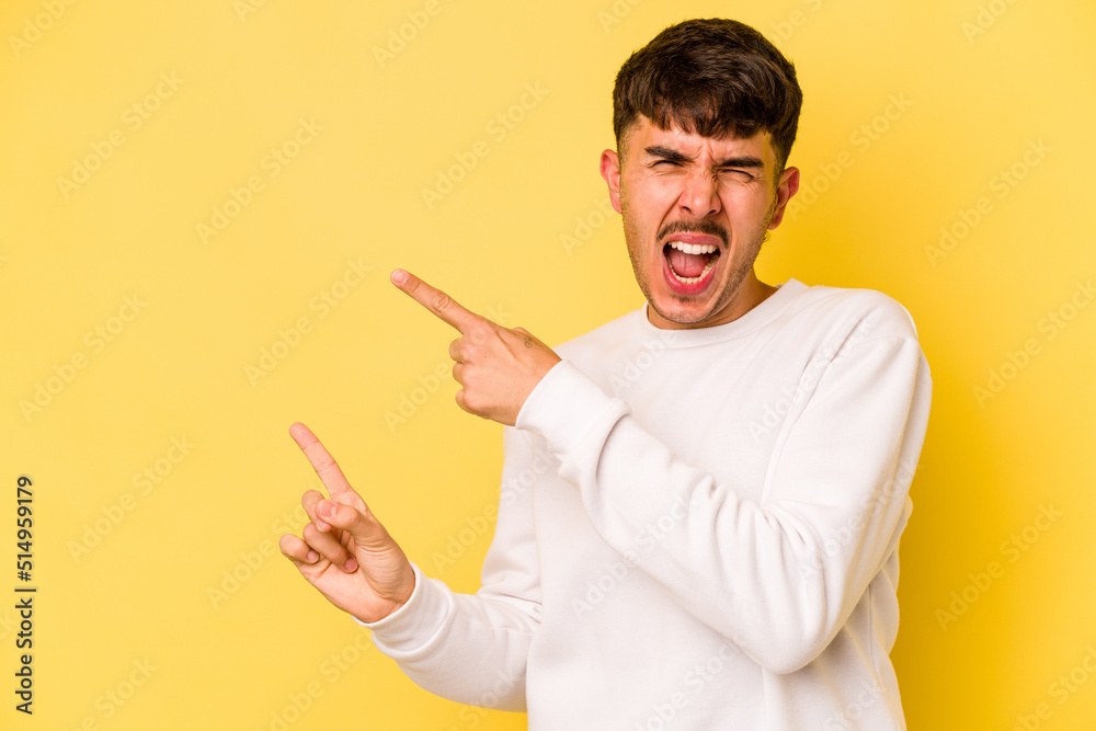 Young caucasian man isolated on yellow background pointing with forefingers to a copy space, expressing excitement and desire.