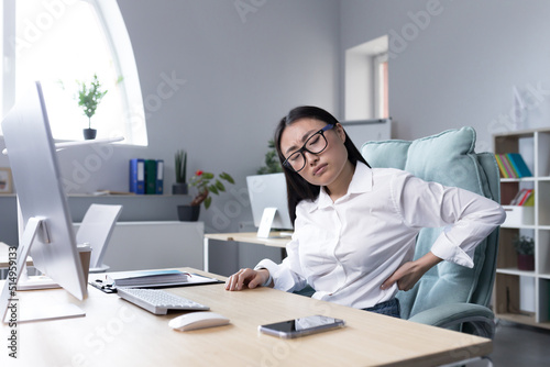 Tired female office worker massaging her back, Asian business woman has severe back and lower back pain.