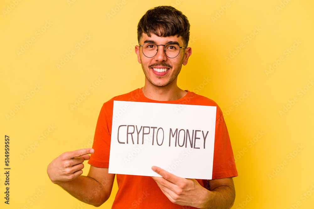 Young hispanic man holding nft placard isolated on yellow background smiling and pointing aside, showing something at blank space. Young hispanic man holding nft placard isolated on yellow background smiling and pointing aside, showing something at blank space.