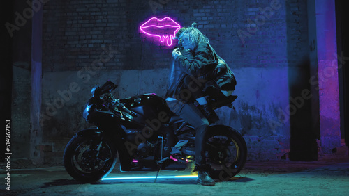 A girl in love and a guy are sitting on a super sport motorcycle flirting and hugging against the background of a neon sign