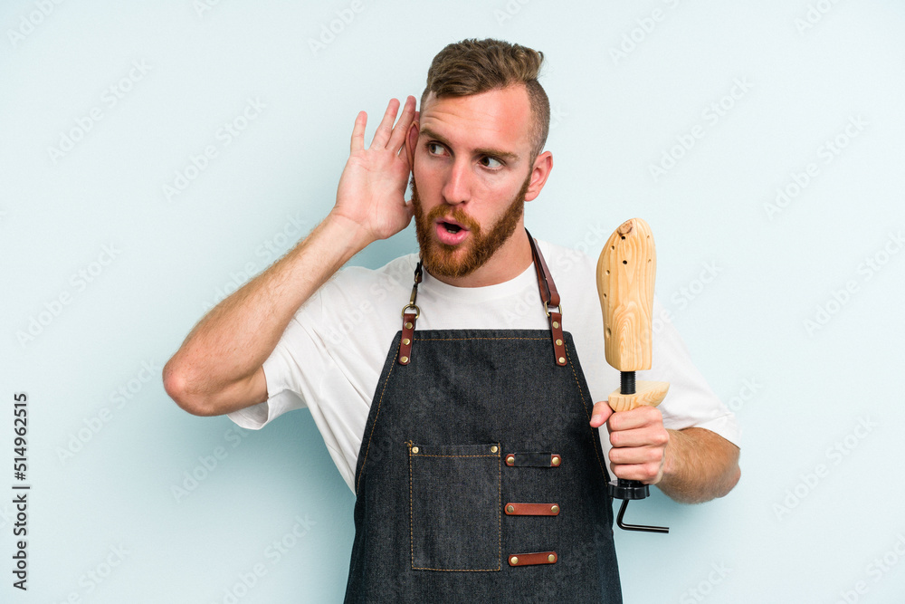 Young caucasian shoe market man isolated on blue background trying to listening a gossip. Young caucasian shoe market man isolated on blue background trying to listening a gossip.