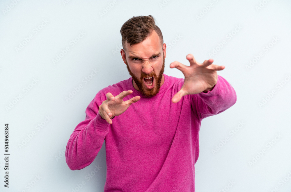 Young caucasian man isolated on blue background showing claws imitating a cat, aggressive gesture. Young caucasian man isolated on blue background showing claws imitating a cat, aggressive gesture.