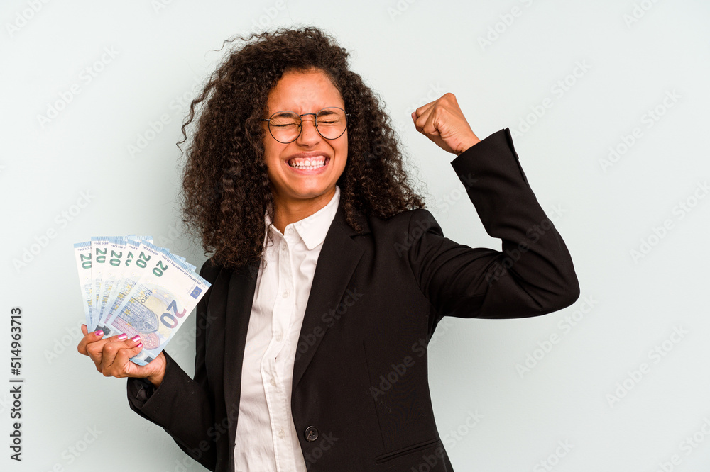 Young business Brazilian woman holding banknotes isolated on white background raising fist after a victory, winner concept. Young business Brazilian woman holding banknotes isolated on white background raising fist after a victory, winner concept.