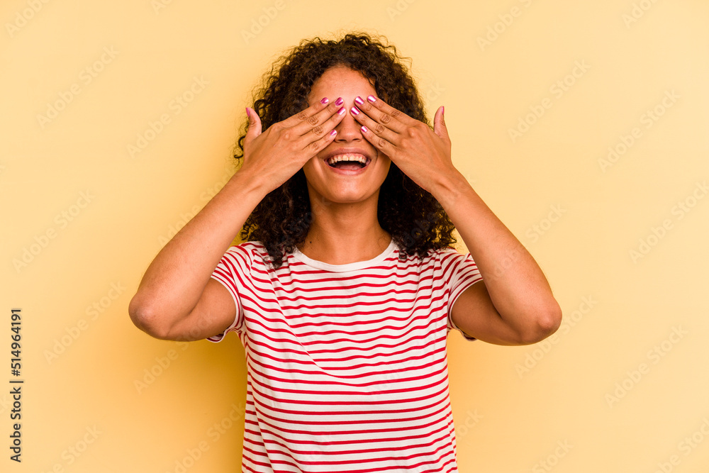 Young Brazilian woman isolated on yellow background covers eyes with hands, smiles broadly waiting for a surprise. Young Brazilian woman isolated on yellow background covers eyes with hands, smiles broadly waiting for a surprise.
