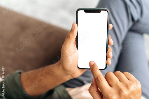 Smartphone in male hands. A man holds his mobile phone in hands with blank white mock-up screen, a place for your advertising, presentation, text, touches the touch screen with his finger. Copy-space