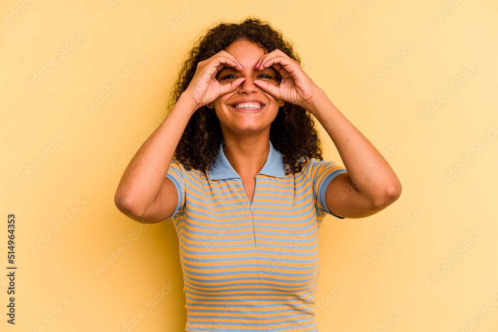Young Brazilian woman isolated on yellow background showing okay sign over eyes Young Brazilian woman isolated on yellow background showing okay sign over eyes