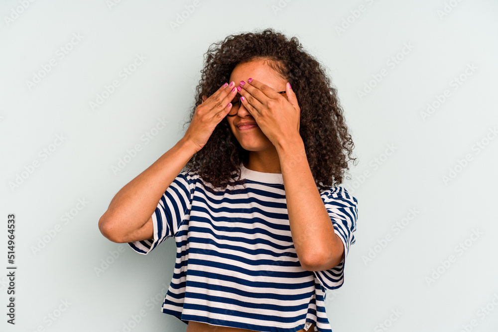 Young Brazilian woman isolated on blue background afraid covering eyes with hands.