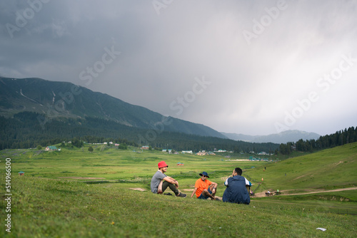 Three Young man tourist relaxing on the Ground, enjoying the panorama with Wetterhorn mountains, glaciers and green fields near Grindelwald, Bernese Oberland, Switzerland, Europe.