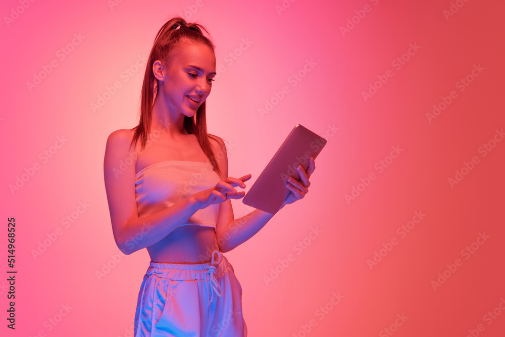 One young charming girl using digital tablet isolated on magenta color background in neon light. Concept of beauty, art, fashion, emotions, youth One young charming girl using digital tablet isolated on magenta color background in neon light. Concept of beauty, art, fashion, emotions, youth