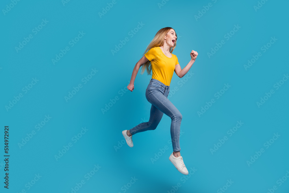 Portrait of sportive active girl in motion jumping over in the air isolated on blue background having perfect stretching