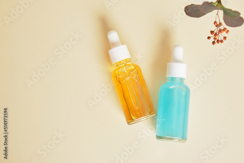 blue and orange serums in transparent dropper bottles on a beige background, natural cosmetics and skin care