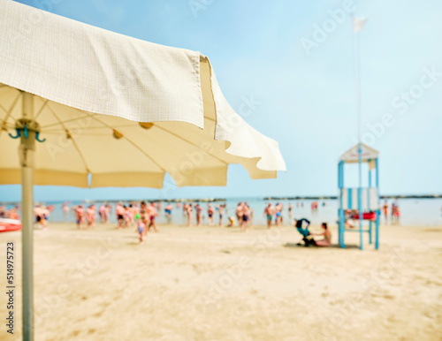 Fototapeta Naklejka Na Ścianę i Meble -  View of the beach from an umbrella with a lifeguard tower alongside a lifeboat on the beach on a sunny summer day, in the background some swimmers refreshing themselves by the Adriatic Sea, Italy.