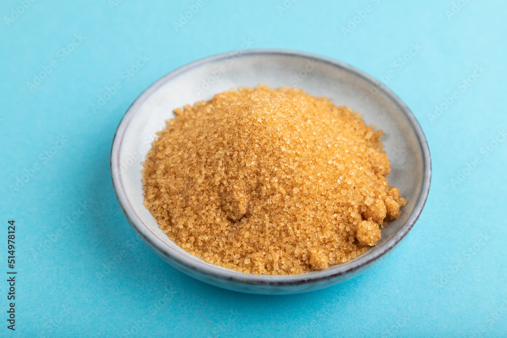 plate with unrefined golden cane sugar on blue pastel. side view, close up. plate with unrefined golden cane sugar on blue pastel. side view, close up.