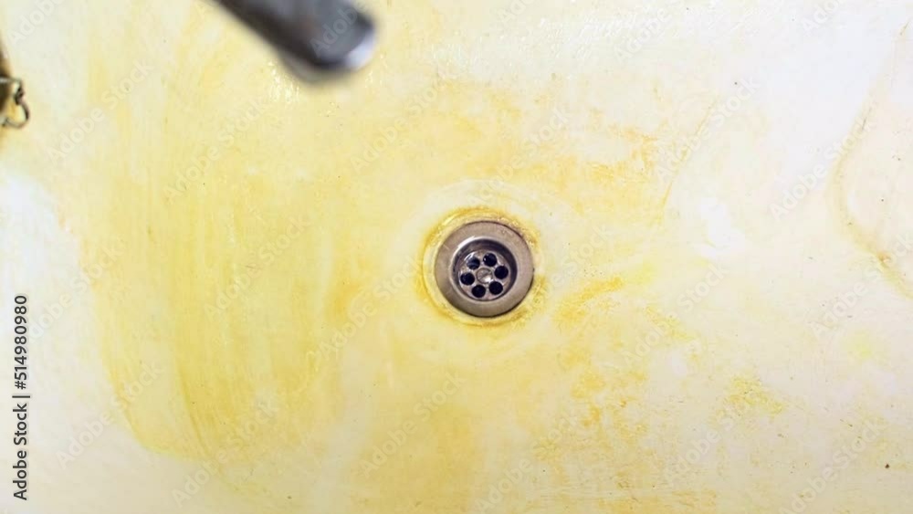 Top view of an old rusty leaking faucet is turned off and dripping drops of water into bathtub with a drain hole. Dirty surface of a bath or sink with a red rust stains. Leak, corrosion, concept.