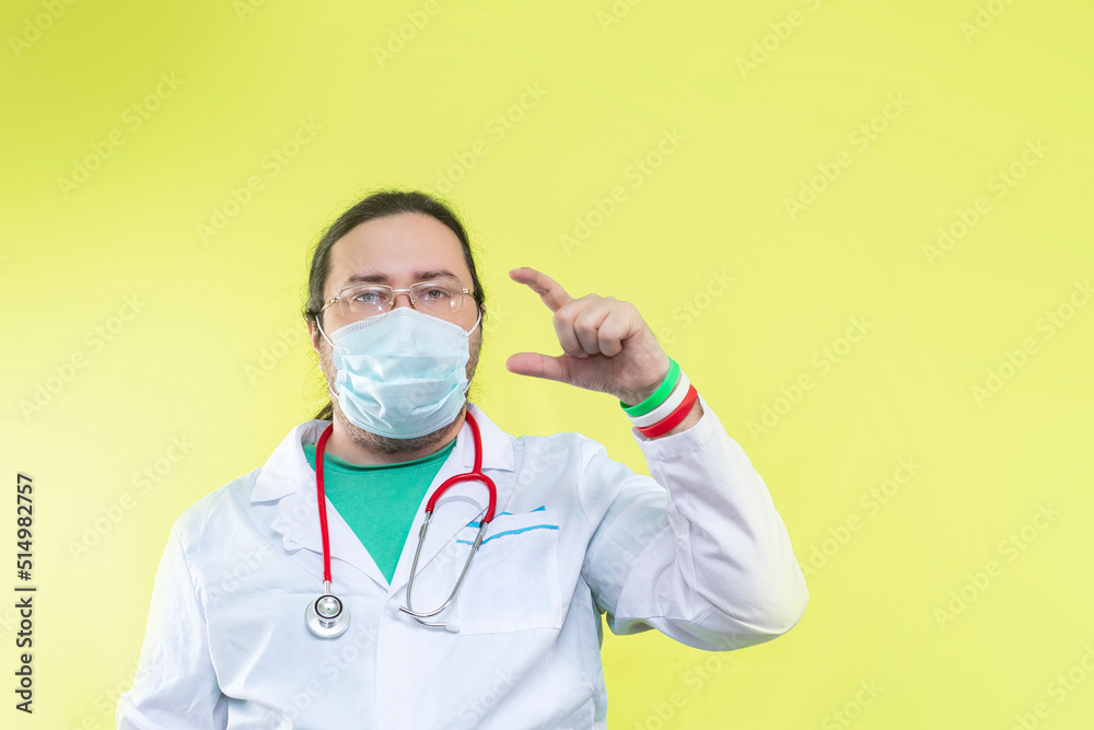A doctor in a white coat and mask shows a small size with his fingers. Bracelet in the colors of the flag of Italy.