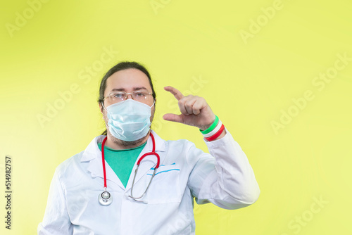 A doctor in a white coat and mask shows a small size with his fingers. Bracelet in the colors of the flag of Italy.
