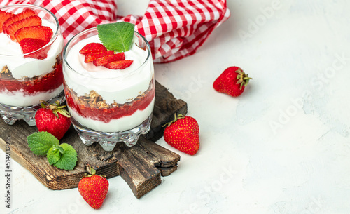 strawberry parfaits with fresh fruit, yogurt and granola on white table, glass jar. Healthy breakfast. Long banner format. top view