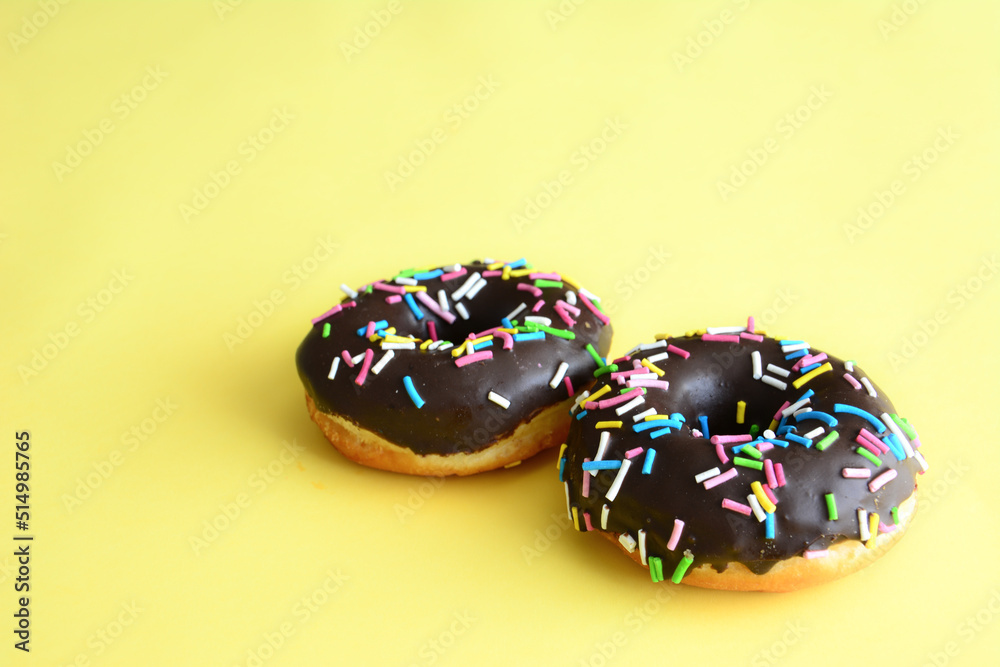 two donuts with chocolate icing and colorful sprinkles on yellow background