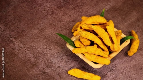 whole turmeric fingers or sticks in a bowl with green leaves on wooden background dark theme,dry turmeric curcuma or halkund rotation photo