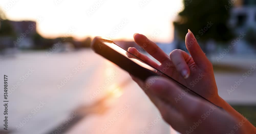 Hands of young woman using smartphone at sunset, close-up Hands of young woman using smartphone at sunset, close-up