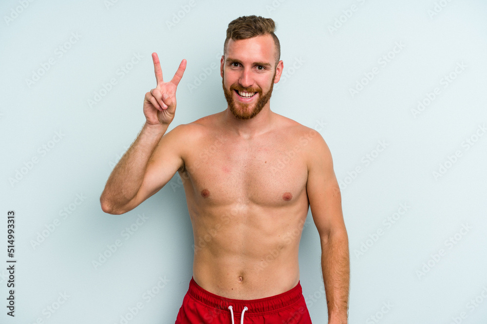Young caucasian man wearing a swimsuit isolated on blue background showing number two with fingers. Young caucasian man wearing a swimsuit isolated on blue background showing number two with fingers.