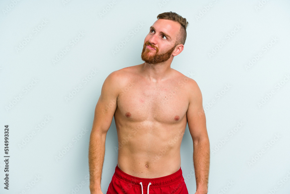 Fototapeta premium Young caucasian man wearing a swimsuit isolated on blue background dreaming of achieving goals and purposes