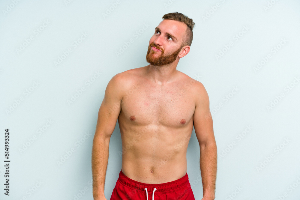 Young caucasian man wearing a swimsuit isolated on blue background dreaming of achieving goals and purposes