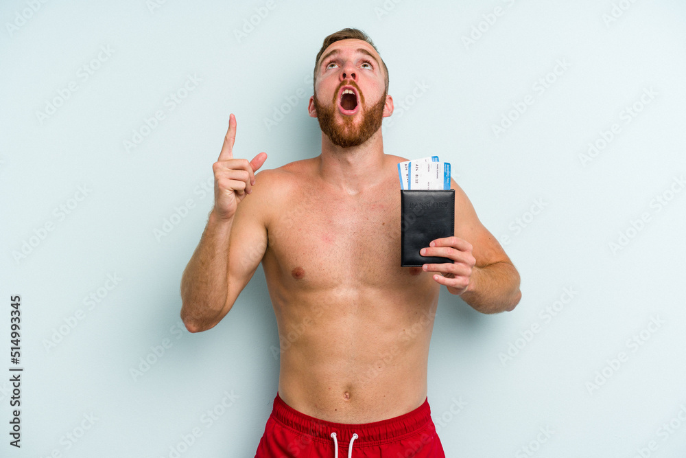 Fototapeta premium Young caucasian man holding a passport isolated on blue background pointing upside with opened mouth.