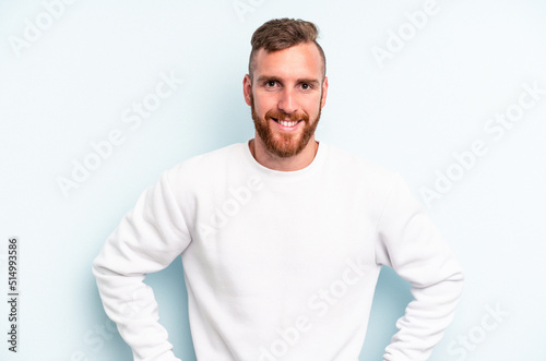 Young caucasian man isolated on blue background confident keeping hands on hips.