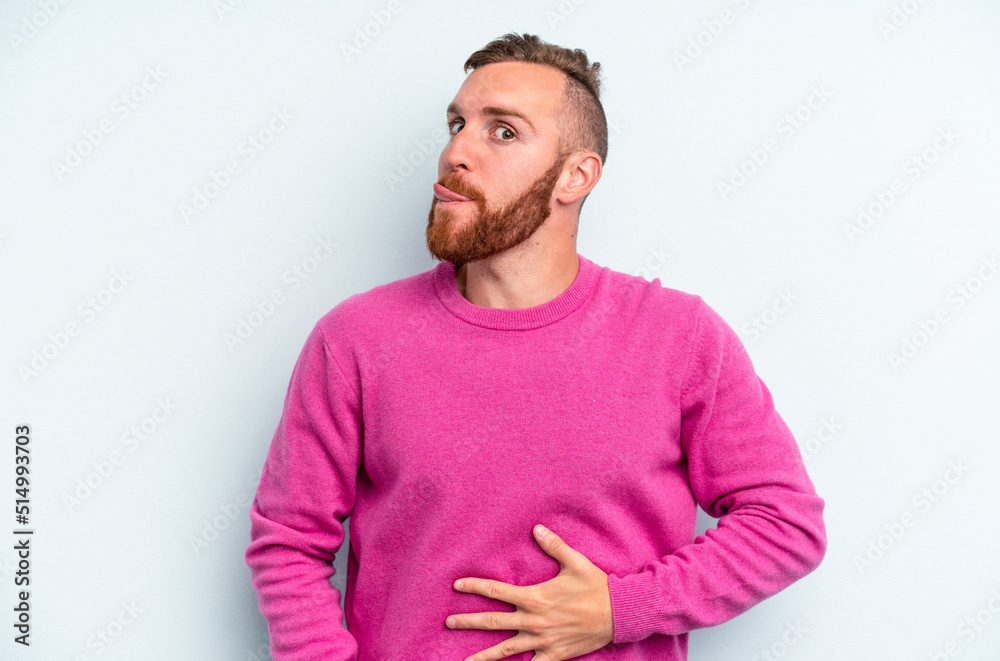 Young caucasian man isolated on blue background touches tummy, smiles gently, eating and satisfaction concept. Young caucasian man isolated on blue background touches tummy, smiles gently, eating and satisfaction concept.