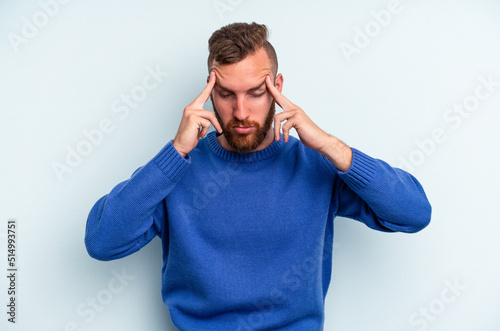 Young caucasian man isolated on blue background having a head ache, touching front of the face.